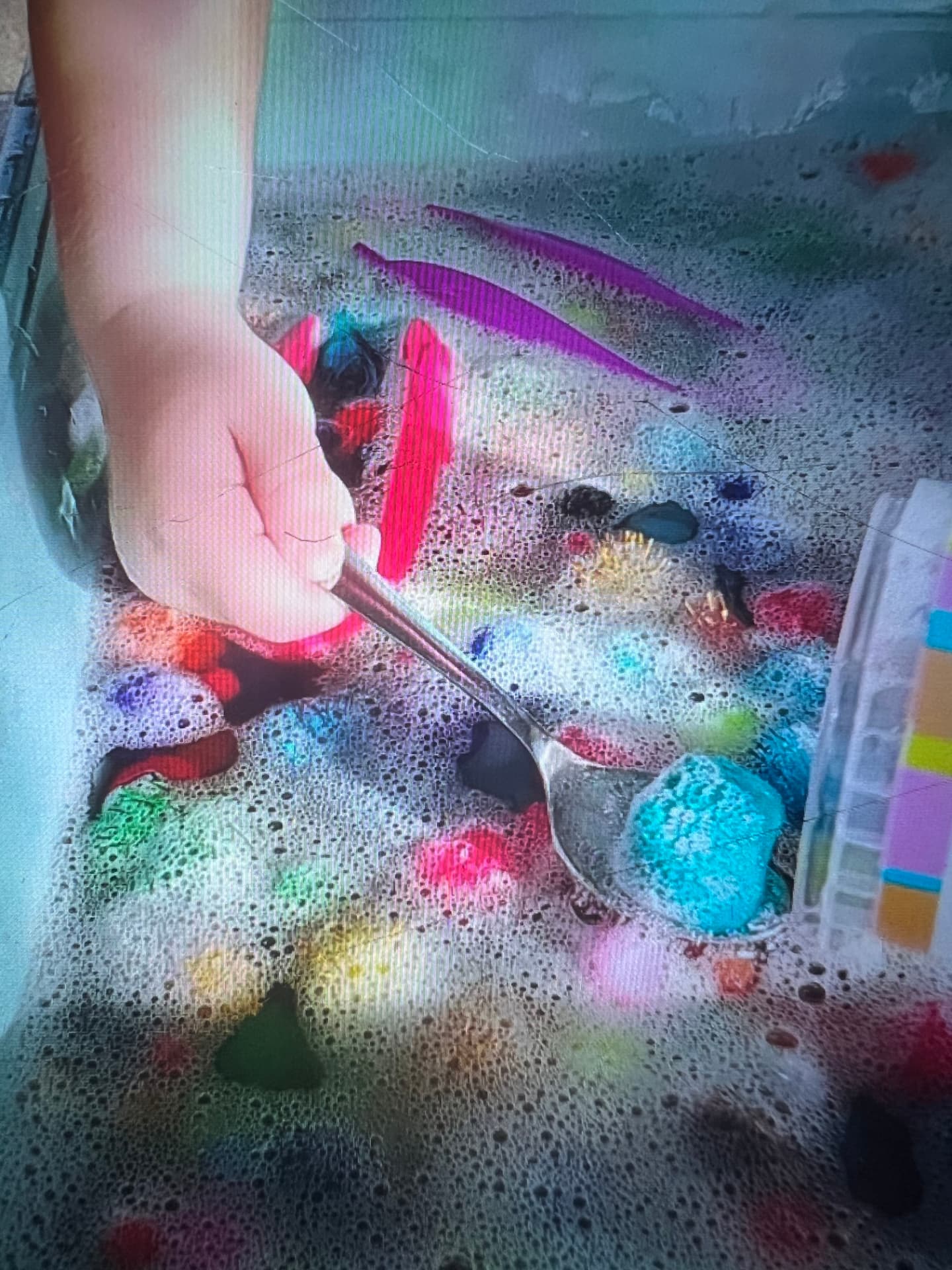 Child drawing lines of pink and purple paint through foam