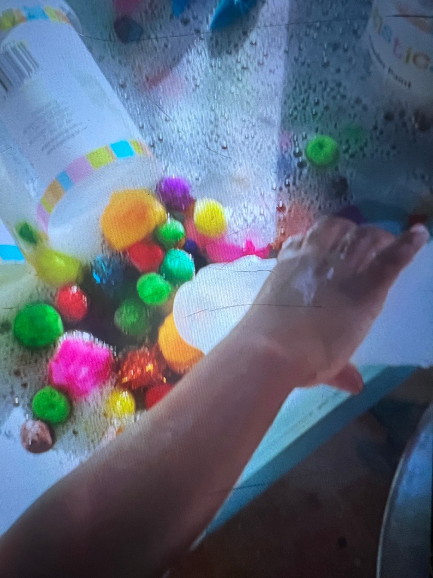 Child's hand exploring pom poms in soapy paint